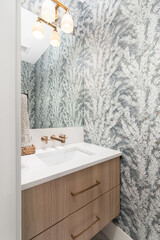 a bathroom with floral wallpaper, a floating wood vanity cabinet, marble countertop, and gold light 