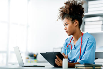 african american female doctor working on laptop, filling out paperwork, patient medical history, re