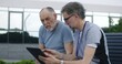 © Framestock - Mature doctor with tablet in hands sits with elderly patient on the bench and consults him. Professional medic in uniform makes diagnosis to client using digital tablet. Medical staff work outdoor.