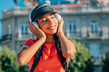 latin urban girl on the street listening to happy music with headphones