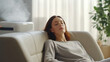 © JKLoma - A beautiful young woman relaxed serene on comfortable sofa rest with air purifier at home.
