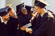 Group of happy and joyful university friends hugging after graduation ceremony. Multiracial young people in mantles and academic caps celebrate university graduation. Education graduation concept.