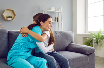 Portrait of a friendly smiling female nurse or doctor woman pediatrician hugging with a child teenage girl patient sitting on sofa at home after medical examination. Health care concept.