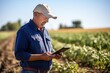 Thoughtful elderly man farmer standing with tablet computer in front of farm 