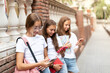 Three teenage girls (14-15 years old) sitting outdoors, absorbed in their phones, exemplify the modern teen (generation Z) lifestyle, education, and the influence of gadgets and social media.