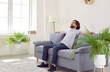 © Studio Romantic - Man is relaxing on the couch at home. Bearded man in polo shirt, jeans and glasses is enjoying a quiet day off and sitting on a comfortable grey sofa in a living room with white walls and green plants
