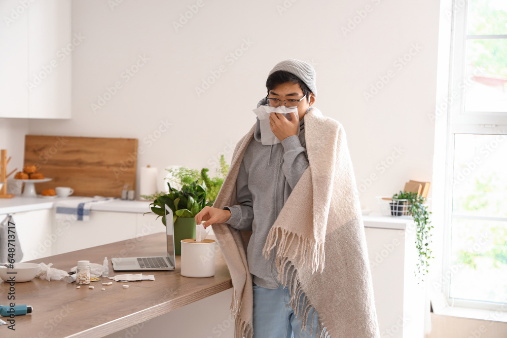 Ill Asian man with tissue in kitchen