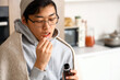 © Pixel-Shot - Ill Asian man taking cough syrup in kitchen, closeup