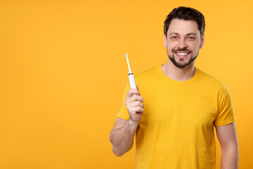 Wall Mural - Happy man holding electric toothbrush on yellow background. Space for text