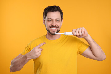 Wall Mural - Happy man holding electric toothbrush on yellow background