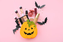 Bag In Shape Of Pumpkin With Makeup Products And Halloween Decor On Pink Background