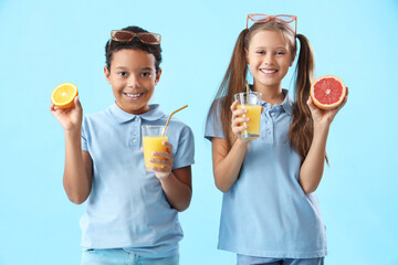 Wall Mural - Little children with glasses of fresh juice and citruses on blue background