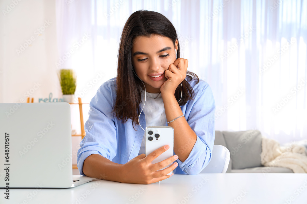 Young woman in earphones using mobile phone at home