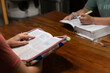 Two women sitting across from each other at table during Bible study with Bibles open, one is holding a highlighter while resting arm on page and the other is pointing to a verse