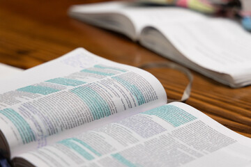 Open Bible laying on table with blue highlighter on pieces of text with another Bible and study book in background