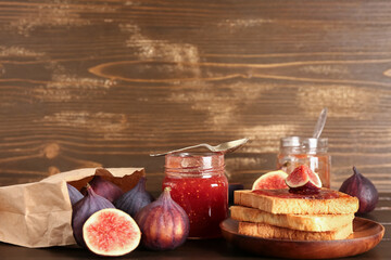 Jar of sweet fig jam and plate with tasty toasts on wooden background