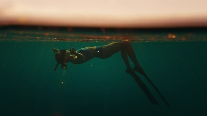 Wall Mural - Woman freediver swims underwater in the sea at sunset and relaxes and floats beneath the surface