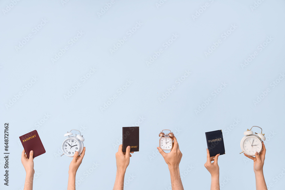 Hands holding alarm clocks and passports on blue background