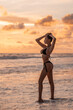 © Detkov D - Slim tanned girl posing against the backdrop of sunset in a separate black swimsuit.