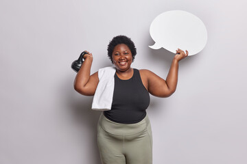 Wall Mural - Plump dark skinned fat woman lifts weight enjoys workout holds blank speech bubble dressed in sportswear does strength workout suggests to write your text here isolated over white background.