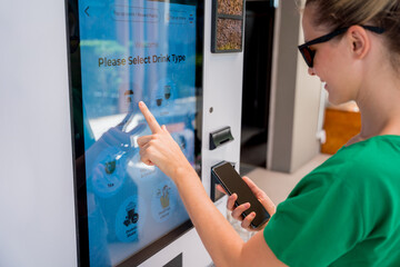 Young woman paying for coffee at vending machine using contactless method of payment 