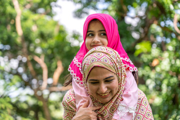 Wall Mural - Portrait of happy religious enjoy happy love asian islam family muslim mother and little muslim girls child with hijab dress smiling and having fun moments good time, islam, ramadan in summer park