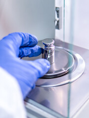 Wall Mural - A operator's hand is holding steel calibration weight to place on the analytical balance. Concept of quality control in a laboratory.