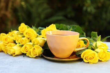 Canvas Print - Cup of drink and beautiful yellow roses on light table outdoors