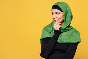 Sticker - Young happy arabian asian muslim woman wear green hijab abaya black clothes put hand prop up on chin look aside isolated on plain yellow background. People uae middle eastern islam religious concept.