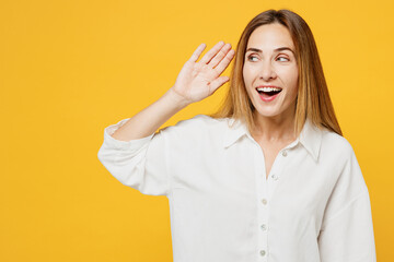 Wall Mural - Young curious nosy caucasian fun happy woman she wearing white shirt casual clothes try to hear you overhear listening intently isolated on plain yellow background studio portrait. Lifestyle concept.