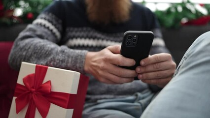 Canvas Print - Young redhead man using smartphone sitting on sofa by christmas decoration at home