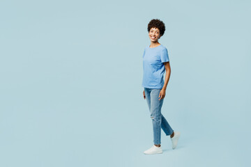 Wall Mural - Full body side profile view young fun woman of African American ethnicity wear t-shirt casual clothes walking going look camera isolated on plain pastel light blue cyan background. Lifestyle concept.