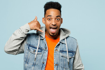 Wall Mural - Young man of African American ethnicity wear denim jacket orange t-shirt doing phone gesture like says call me back isolated on plain pastel light blue background studio portrait. Lifestyle concept.