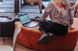 © qunica.com - Muslim female employee wearing hijab working on financial statistics at the office while sitting on orange sofa. Back view shot. Cropped photo