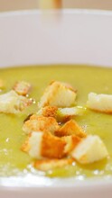 Vertical Video. Close Up Of Pieces Of Dried White Bread Falling Into The Cream Soup. Serving First Courses With Crackers.