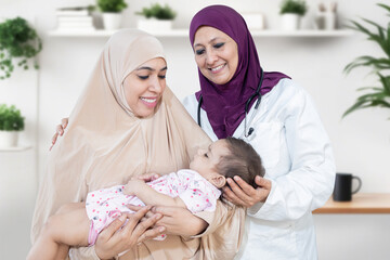 Wall Mural - Happy Young arab mother wearing with her cute little baby visiting general pediatrician in modern clinic for routine check-up, Healthcare and medical concept. Women wearing headscarf.