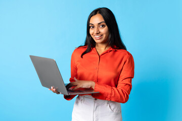 Wall Mural - Indian Woman Using Laptop Computer Typing On Blue Studio Background