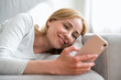 © brizmaker - Woman relaxing on comfortable couch, holding smartphone in hands