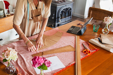 DRESSMAKER AT HER WORK TABLE WITH PATTERNS AND FABRICS