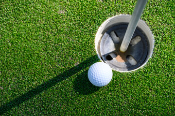 Wall Mural - Closeup of white golf ball next to the cup on a putting green
