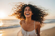 Woman with curly hair is captured smiling on beach. This picture can be used to depict happiness, relaxation, vacations, or summer vibes.