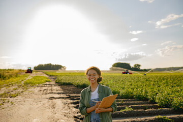 Wall Mural - Female agronomist standing with clipboard on field during harvesting. Agricultural concept