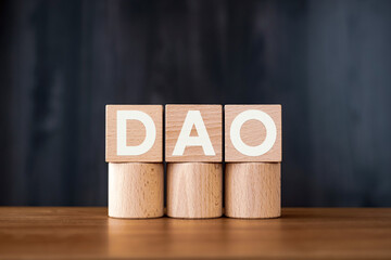 Poster - There is wood cube with the word DAO. It is an abbreviation for Decentralized Autonomous Organization as eye-catching image.