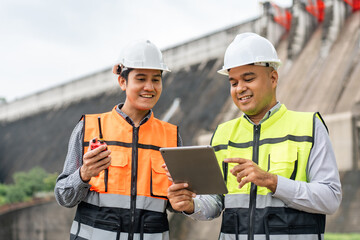 Confident asian two maintenance engineers man inspection discussstion with tablet at construction site dam with hydroelectric power plant and irrigation. Team engineer man working at project