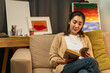 © Chanakon - Asian beautiful woman sitting reading book on cozey couch sofa in living room with warm light at night. People female stay home part time relax at home.