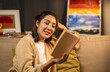 © Chanakon - Asian beautiful woman sitting reading book on cozey couch sofa in living room with warm light at night. People female stay home part time relax at home.