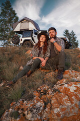 Couple of girl and guy of travelers with car with tent on roof in mountains.