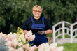 Happy senior woman gardener use computer tablet for care flowers. Farmer control garden shop with modern technologies