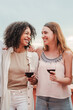 Vertical portrait of two young female friends having fun talking and drinking wine. Adult women smiling and holding wineglasses at party celebration. Ladies or girls smiling with alcohol glasses. High