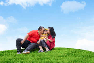 Wall Mural - Happy asian family sitting on the grass over beautiful blue sky